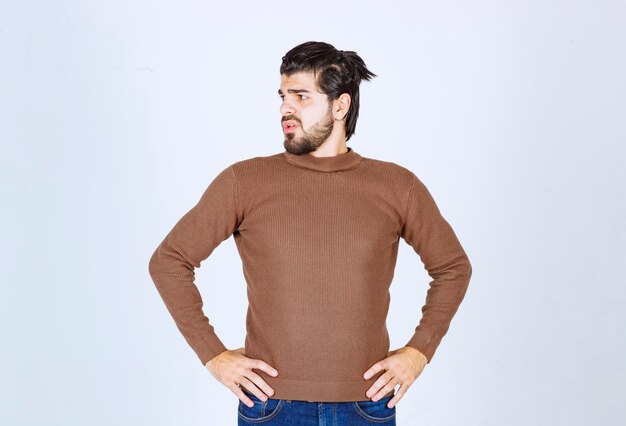 Photo d'un modèle de jeune homme séduisant debout avec les mains sur les hanches et regardant au loin sur un mur blanc. photo de haute qualité