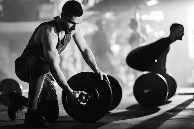 Photo en noir et blanc d'un homme athlétique ajustant des haltères sur la musculation dans un club de santé
