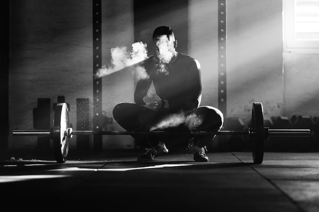 Photo en noir et blanc d'un homme musclé utilisant de la craie de sport avant de soulever une barre sur la musculation dans une salle de sport