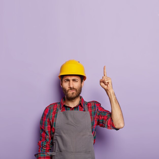 Photo d'un ouvrier mécanique mal rasé portant un casque de chantier et un uniforme spécial