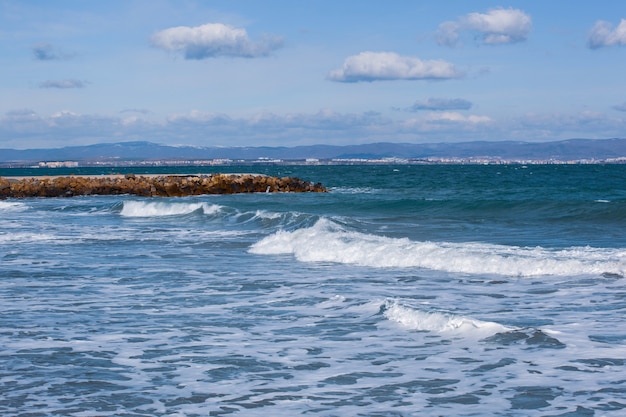 Photo panoramique d'un océan avec des vagues qui roulent et un quai de pierre sous un ciel nuageux