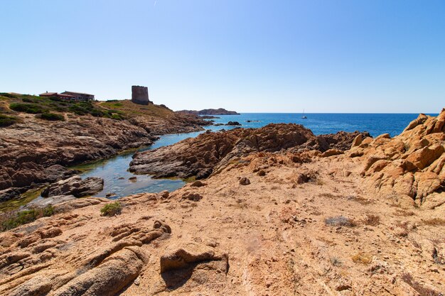 Photo de paysage d'un bord de mer avec de gros rochers sur la colline dans un ciel bleu clair