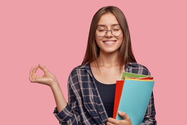 Photo d'une petite amie joyeuse satisfaite, médite après avoir eu des cours, ferme les yeux avec plaisir, fait un geste correct