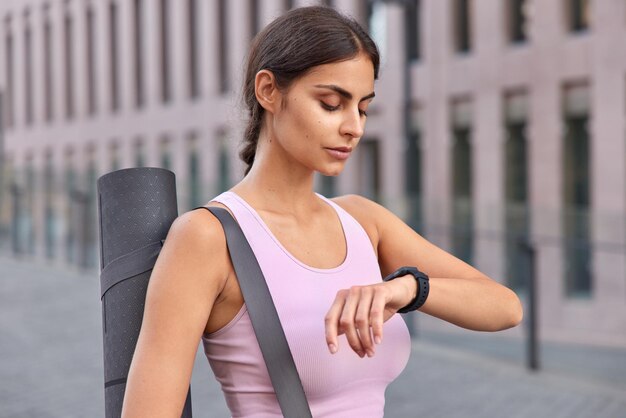 Une photo en plein air d'une jeune femme active vérifie les résultats de remise en forme sur une montre de remise en forme porte un karemat vêtu de vêtements de sport