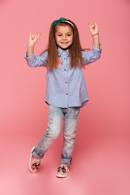 Photo pleine longueur de drôle de petite fille gesticulant rock sign avec deux mains