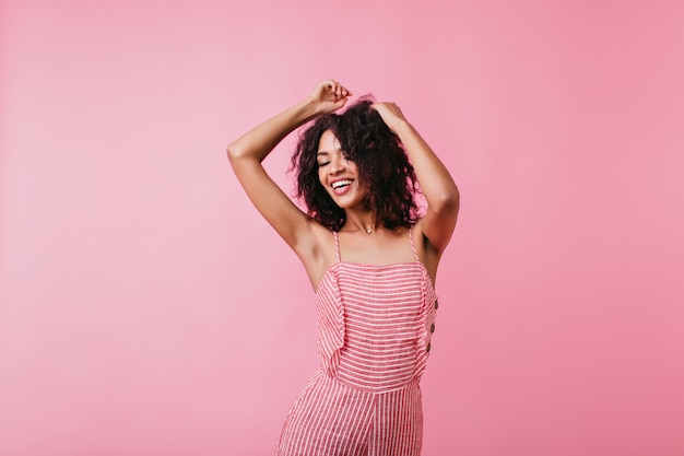 Photo prise d'une danseuse en haut rayé doux. Modèle de bonne humeur pose les bras levés.