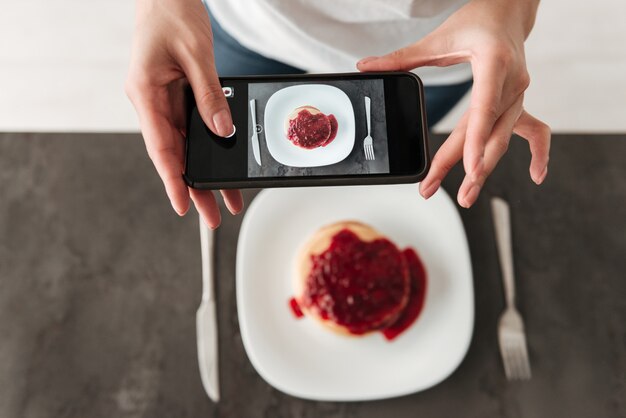 Photo recadrée d'une femme faire une photo de crêpes par téléphone.