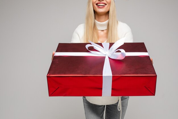 Photo recadrée de femme heureuse dans un pull blanc tenant une grande boîte-cadeau