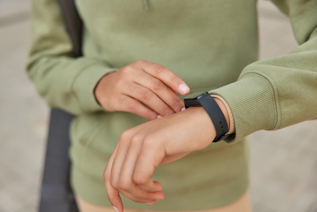 Une photo recadrée d'une femme inconnue sans visage utilise une montre intelligente moderne pour suivre ses performances d'entraînement surveille les progrès et porte des poses de sweat-shirt vert sur fond flou. Concept de mode de vie sain