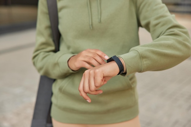 Une photo recadrée d'une femme inconnue vérifie les résultats de la condition physique sur les moniteurs de smartwatch, le pouls vêtu d'un sweat-shirt décontracté porte des poses de karemat à l'extérieur