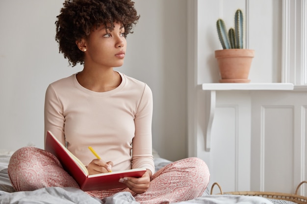 Photo gratuite photo recadrée d'une femme à la peau sombre est assise jambes croisées, porte un pyjama