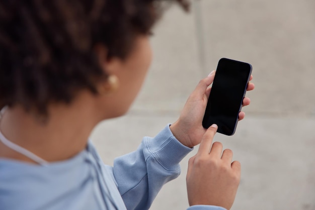 Une photo recadrée d'une femme sans visage en sweat à capuche utilise un téléphone portable avec un écran de simulation pour votre message texte ou votre contenu d'information vêtu d'un sweat à capuche décontracté et contient un gadget numérique moderne. Notion de technologie