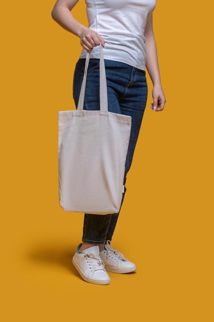 Photo recadrée d'une femme vêtue d'un t-shirt et d'un jean tenant son sac tendance dans une main