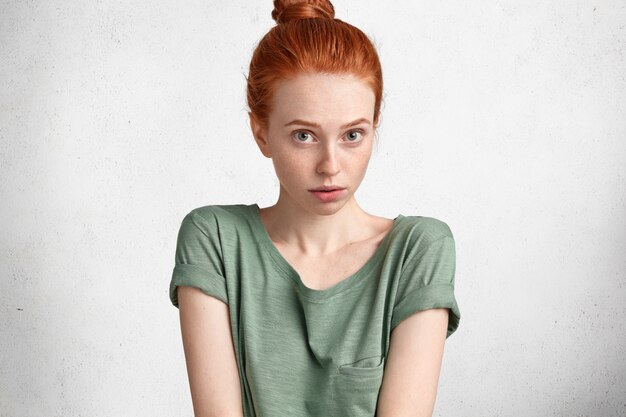 Photo recadrée d'une jeune femme rousse à la recherche agréable vêtue de vêtements décontractés, a déplu et surpris l'expression, isolée sur blanc