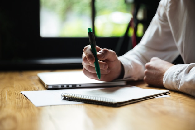 Photo recadrée de la main de l'homme tenant un stylo vert, tout en prenant des notes