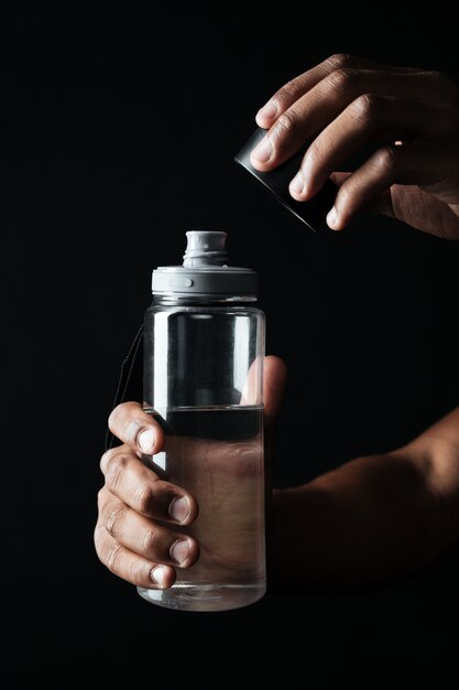 Photo recadrée de mains d'hommes afro-américains ouvrir la bouteille avec de l'eau