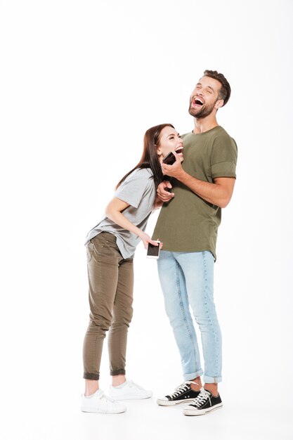 Photo de rire jeune couple d'amoureux debout isolé. Regardant de côté et tenant les téléphones.