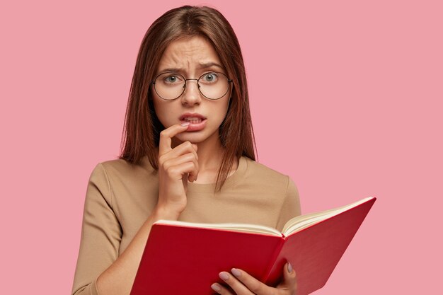 Photo de Studio d'une femme aux cheveux noirs mécontente fronce le visage, garde l'index près de la bouche, se sent insatisfaite