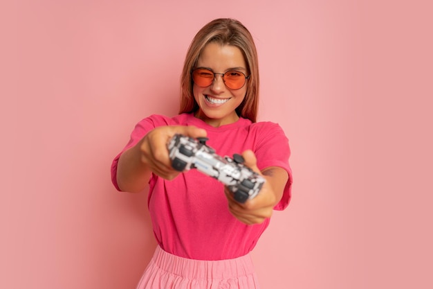 Photo de studio d'une femme souriante folle excitée et heureuse jouant à des jeux vidéo accro à la playstation isolée sur fond de couleur rose