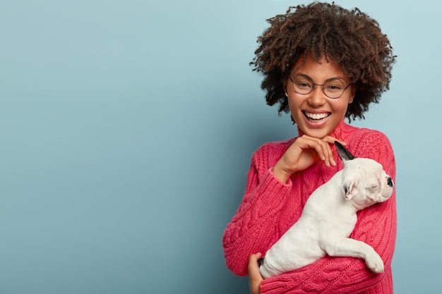 Photo De Studio De Fille Afro-américaine Optimiste Touche Doucement Le Menton, Vêtue D'un Pull Rose