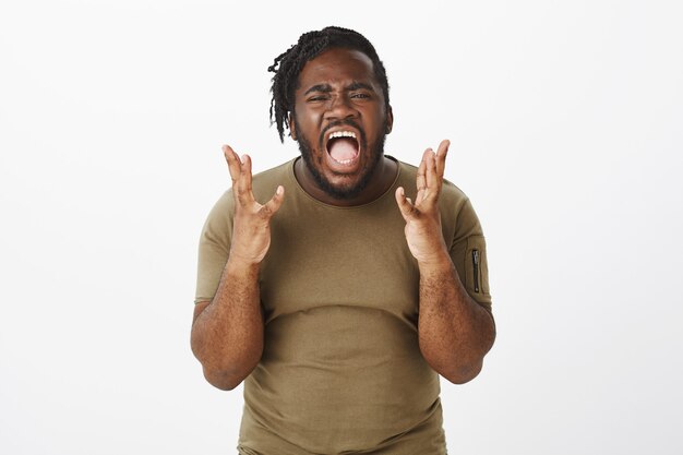 Photo de Studio de gars ennuyé dans un t-shirt marron posant contre le mur blanc