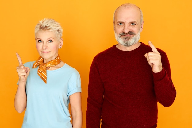 Photo gratuite photo de studio de grand-père barbu en colère et de grand-mère mécontente fronçant les sourcils faisant un geste d'avertissement en gardant les doigts avant levés.