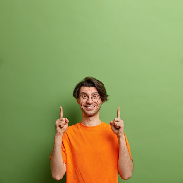 Photo de Studio d'heureux homme européen mal rasé avec une expression positive pointe vers le haut sur un espace vide