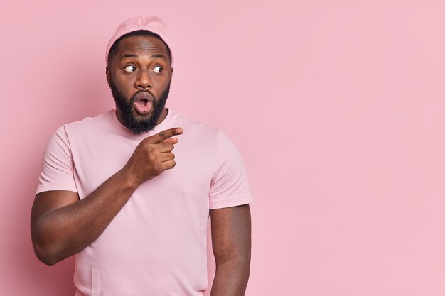 Photo de Studio de l'homme afro-américain barbu choqué pointe de côté sur l'espace de copie montre quelque chose d'incroyable habillé avec désinvolture objet isolé sur mur rose