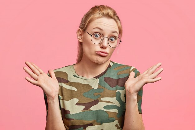 Photo de Studio de jeune femme blonde hésitante avec une expression incertaine, hausse les épaules, se sent l'hésitation concernant la prise de décision, isolée sur rose