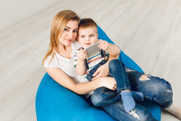 Photo de Studio d'une mère tenant son enfant dans les bras. Garçon joue sur smartphone et sourit