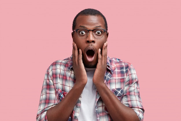 Photo gratuite photo de studio de peur terrifié client africain à la peau sombre choqué par les prix au magasin, étant à court d'argent pour acheter quelque chose, isolé sur rose