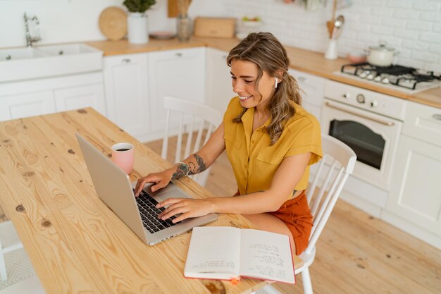 Photo de style de vie intérieur d'une femme au foyer heureuse cherchant des reçus et buvant du café dans une cuisine moderne et légère