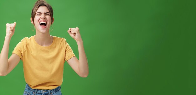 Photo gratuite une photo de taille d'une femme charismatique, énergique et excitée en t-shirt jaune, fermant les yeux et criant: