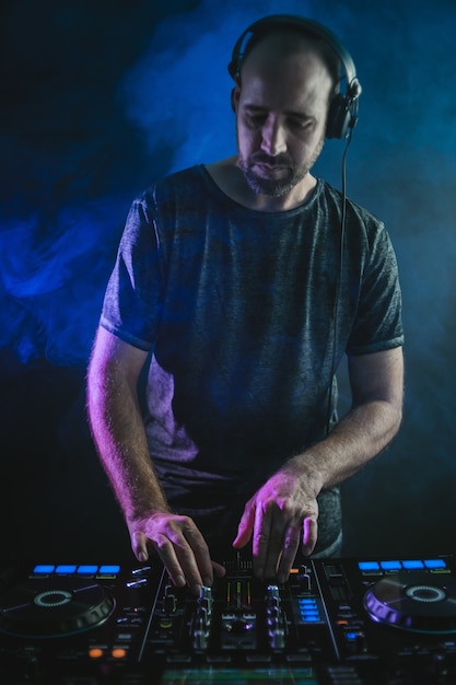 Photo verticale d'un DJ masculin sous les lumières bleues et fumée