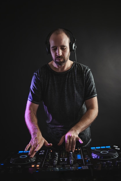 Photo verticale d'un DJ masculin travaillant sous les lumières contre un noir dans un studio