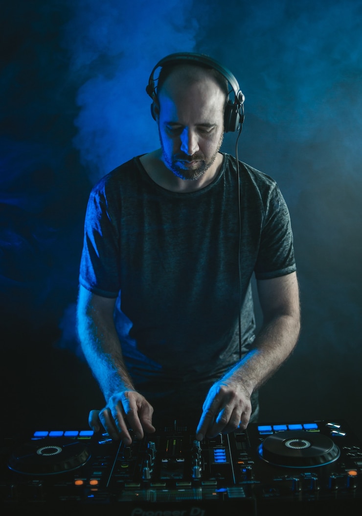 Photo gratuit photo verticale d'un dj masculin travaillant sous les lumières contre un noir
