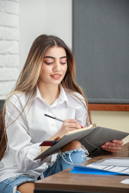 Photo verticale d'une jeune femme prenant des notes assise au bureau Photo de haute qualité