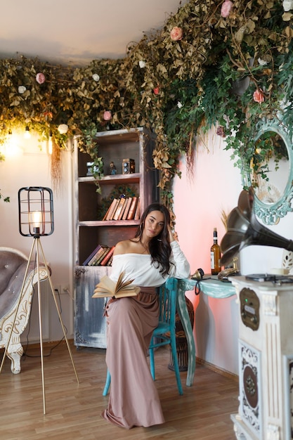 Photo gratuite photo verticale d'une jeune fille assise sur une chaise et lisant un livre photo de haute qualité