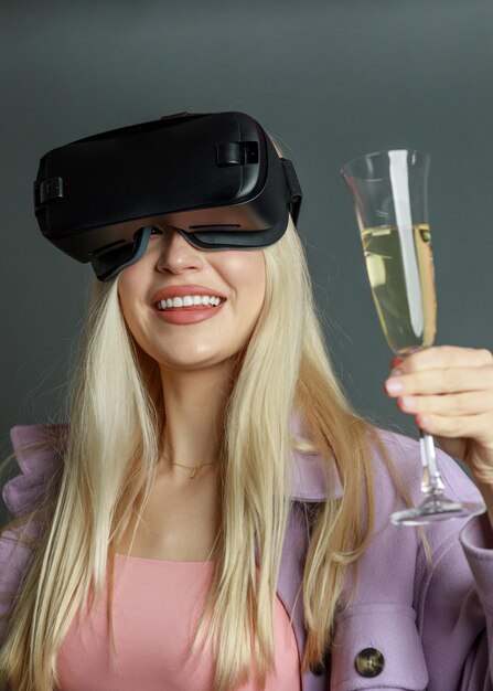 Photo verticale d'un jeune joueur blond portant un ensemble VR et tenant une coupe de champagne