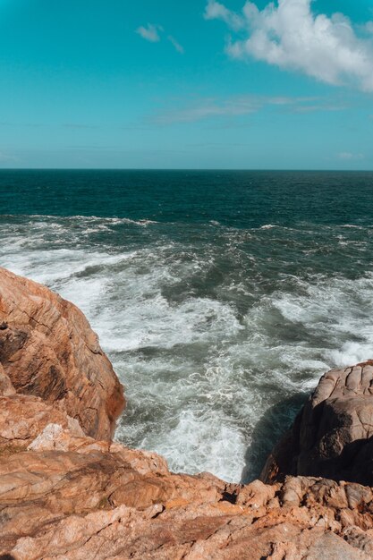 Photo verticale de roches entourées par la mer sous un ciel bleu et la lumière du soleil