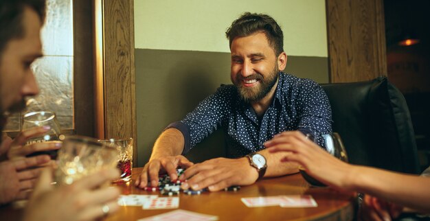 Photo vue latérale d'amis assis à une table en bois. Amis s'amusant en jouant au jeu de société.