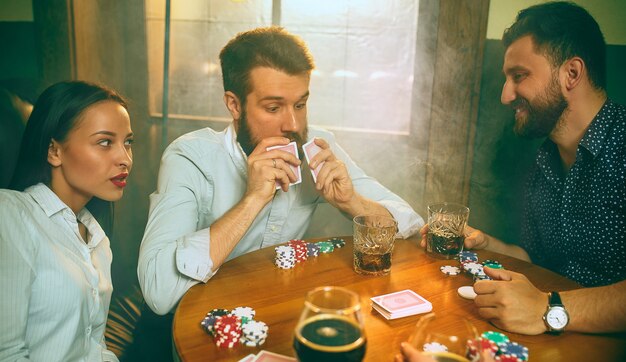 Photo vue latérale d'amis assis à table en bois. Amis s'amusant tout en jouant au jeu de société.