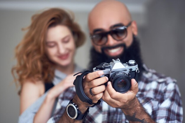 Photographe barbu amateur et une femme rousse posant sur fond gris clair.