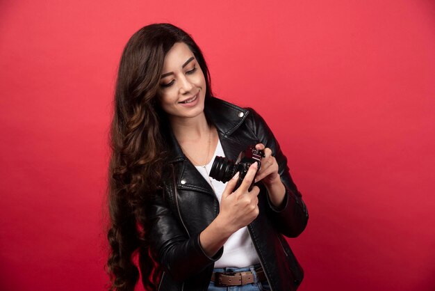 Photographe de belle femme regardant sur un appareil photo sur fond rouge. photo de haute qualité