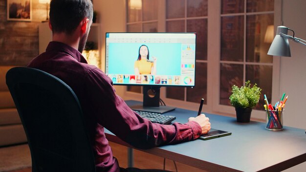 Photographe masculin éditant des photos au bureau la nuit à l'aide d'une tablette graphique.