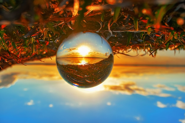 Photographie de boule de lentille de cristal créative de verdure et d'un lac au coucher du soleil