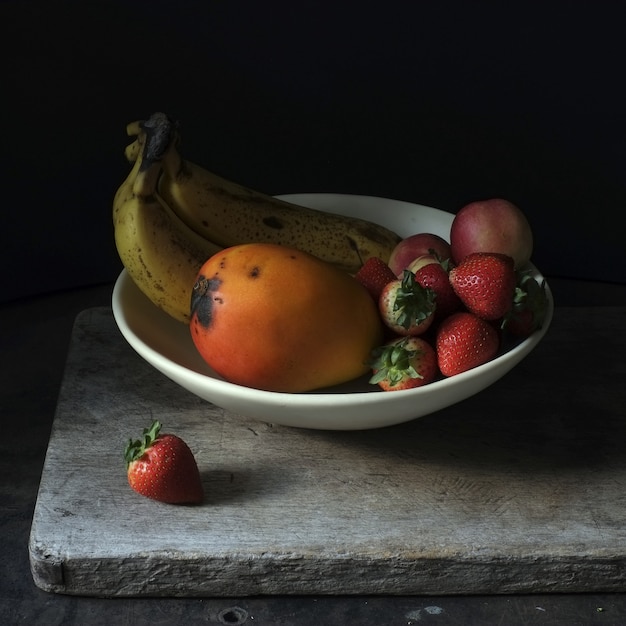 Photo gratuite photographie de nature morte de fruits frais dans une assiette blanche sur fond noir