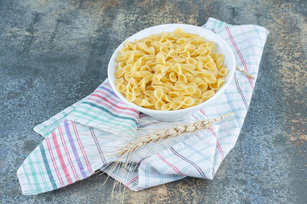 Épi de blé à côté d'un bol de pâtes farfalle , sur la surface en marbre.