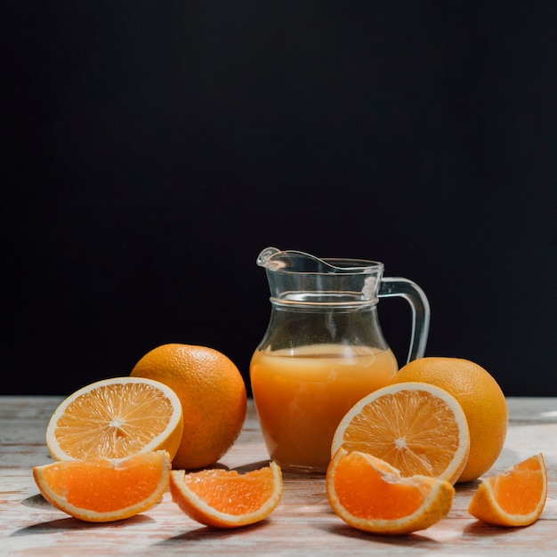 Pichet de délicieux jus d'orange entouré de verres et d'oranges vue de face