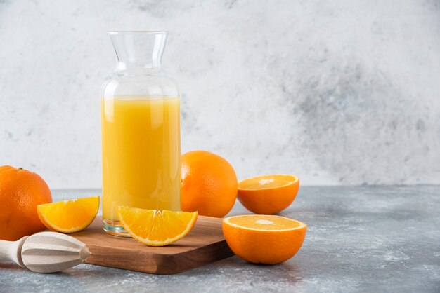 Pichet en verre de jus avec des fruits orange frais sur une planche de bois.